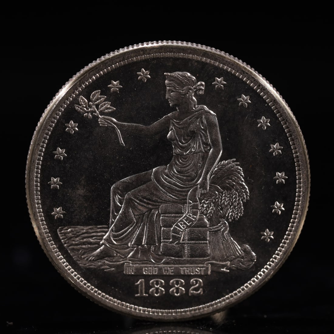 USA Trade Dollar 1882 Coin: American coin. Obverse: Liberty seated on a pedestal facing the sea to the left holding olive branches surrounded by 13 stars. IN GOD WE TRUST / LIBERTY / 1882. Reverse: An eagle holding branches