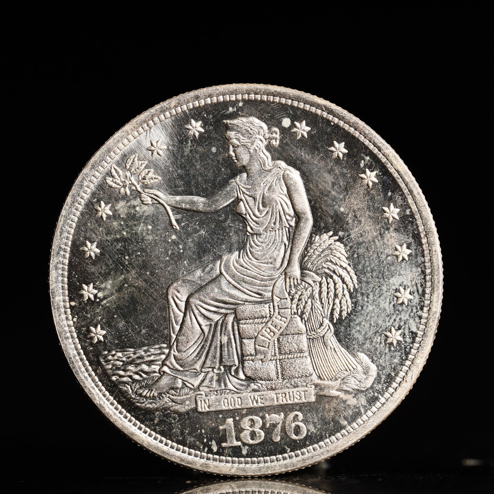 USA Trade Dollar 1876 Coin: American coin. Obverse: Liberty seated on a pedestal facing the sea to the left holding olive branches surrounded by 13 stars. IN GOD WE TRUST / LIBERTY / 1876. Reverse: An eagle holding branches with