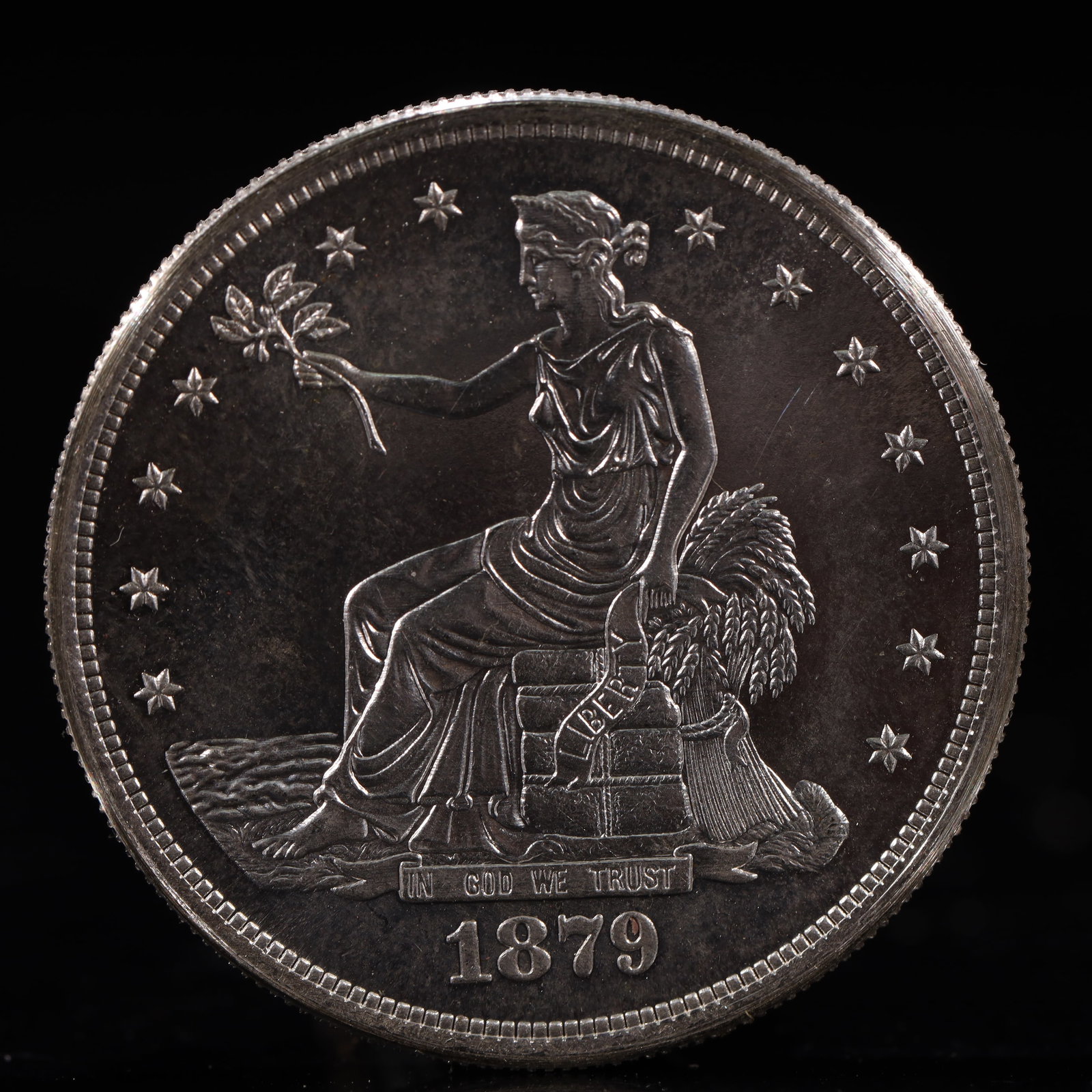 USA Trade Dollar 1879 Coin: American coin. Obverse: Liberty seated on a pedestal facing the sea to the left holding olive branches surrounded by 13 stars. IN GOD WE TRUST / LIBERTY / 1879. Reverse: An eagle holding branches with
