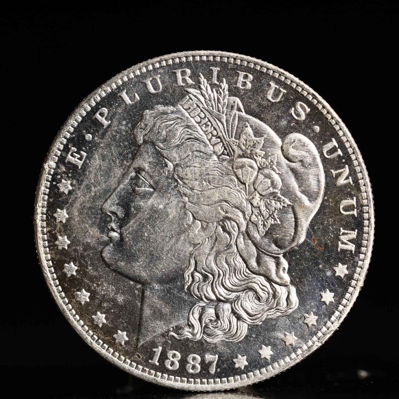 USA Morgan Dollar 1887 Coin: Obv: profile bust with date below and E PLURIBUS UNUM legend and stars around. Rev: eagle with In God we trust above within wreath with UNITED STATES OF AMERICA ONE DOLLAR legend. IN GOD WE TRUST / LI