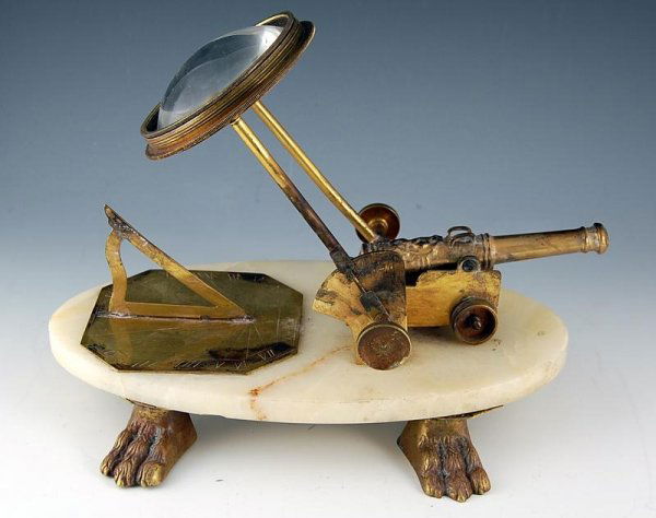 Sundial/Signal Cannon: Sundial instrument mounted on white onyx base with brass lion's paw feet; sunlight concentrating lens, fixed on touch hole of brass cannon to ignite a black powder charge at a specific time. 9"H x 12"