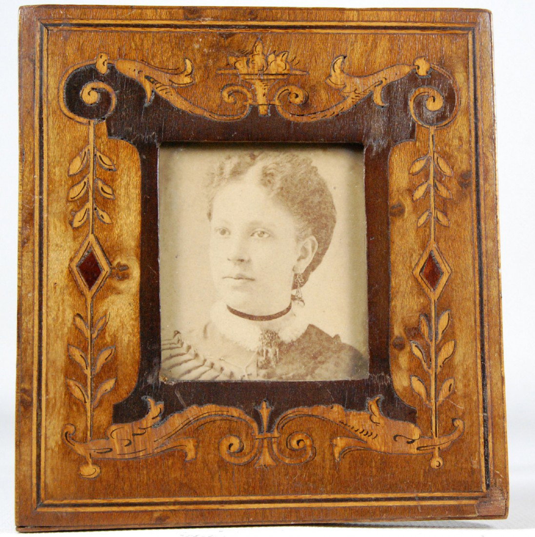 Frame, tabletop, inlaid dolphins Wood tabletop fam: Wood tabletop fame with inlaid decoration of dolphins at bottom and leading to a crown of compote and fruit. The original albumen photo of a woman by Loomis, Boston. C. 1870-80. Size: 4" H x 3.75" W W