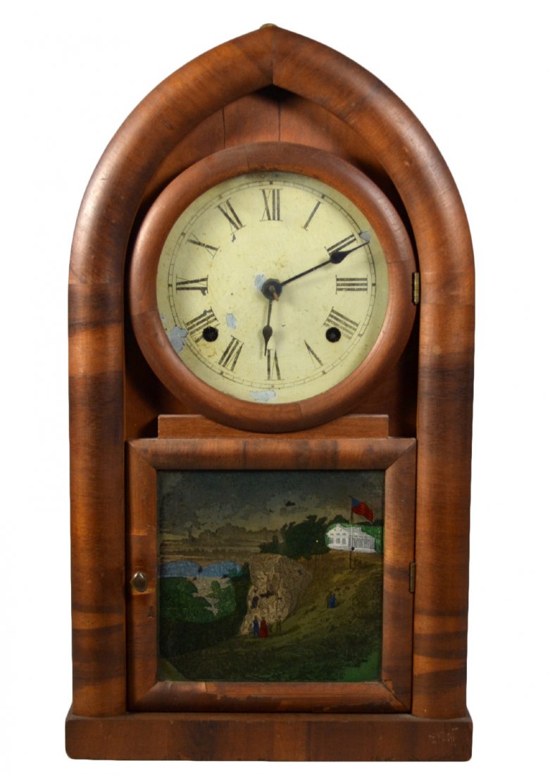 Clock, Waterbury, Landscape w/American flag: A steeple shaped top, Waterbury Clock with a landscape scene, printed, flying an American flag on the glass of the case. All original paper liner and original paint on face. Size: 18.75" H. x 10.5" W.