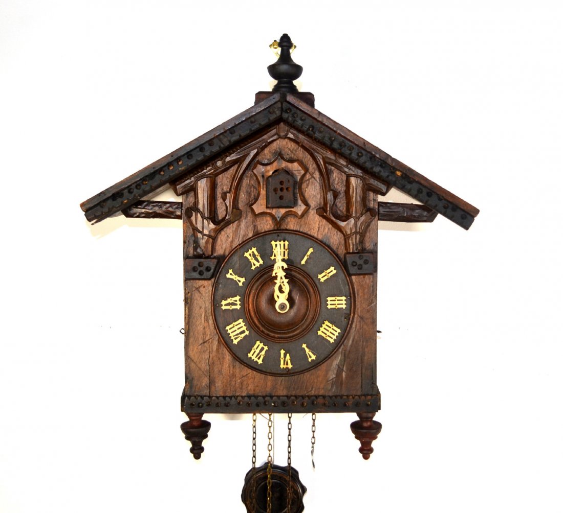 Clock, Cuckoo, gable roof, carved trees: Cuckoo Clock with carved tree trunks and rake boards and single finial on top. Celluloid numbers and hands, acorn weights.. Germany early 20th century. Size: 19" H. x 16" W. x 7.75" D. Weight: 12lbs