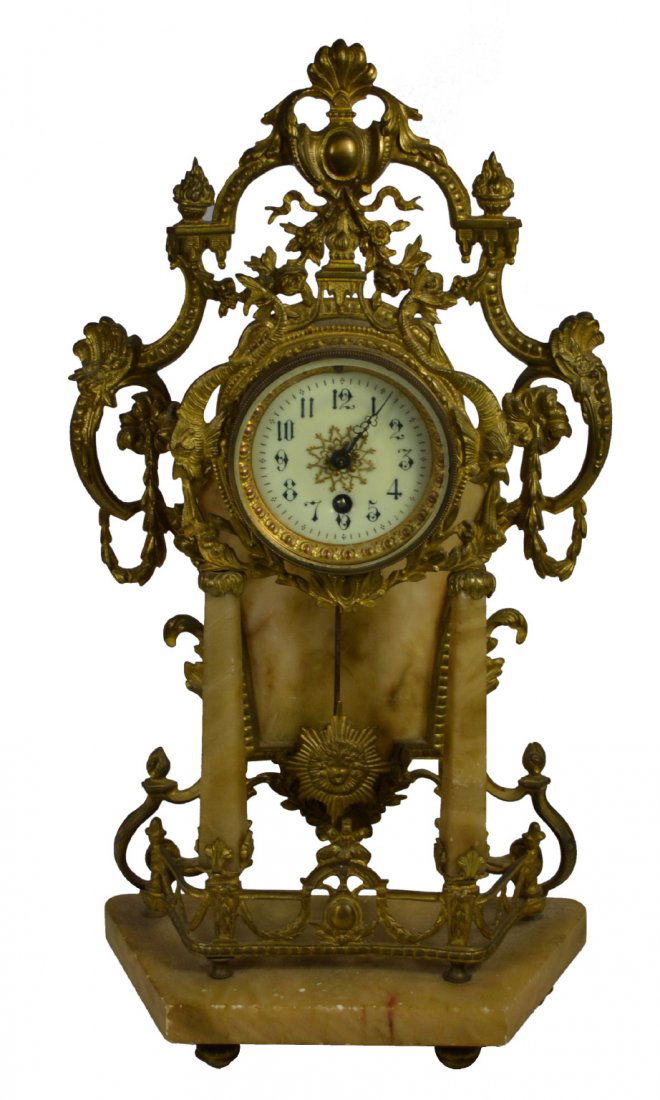 Clock, Brass Surround, Alabaster, Circa 1900: Shelf clock. Material: Brass, alabaster & porcelain. Construction: Cast brass. Period: Circa 1900. Features: Clock has an ornate brass surround depicting flowers, foliates, torches, fish and scroll wo