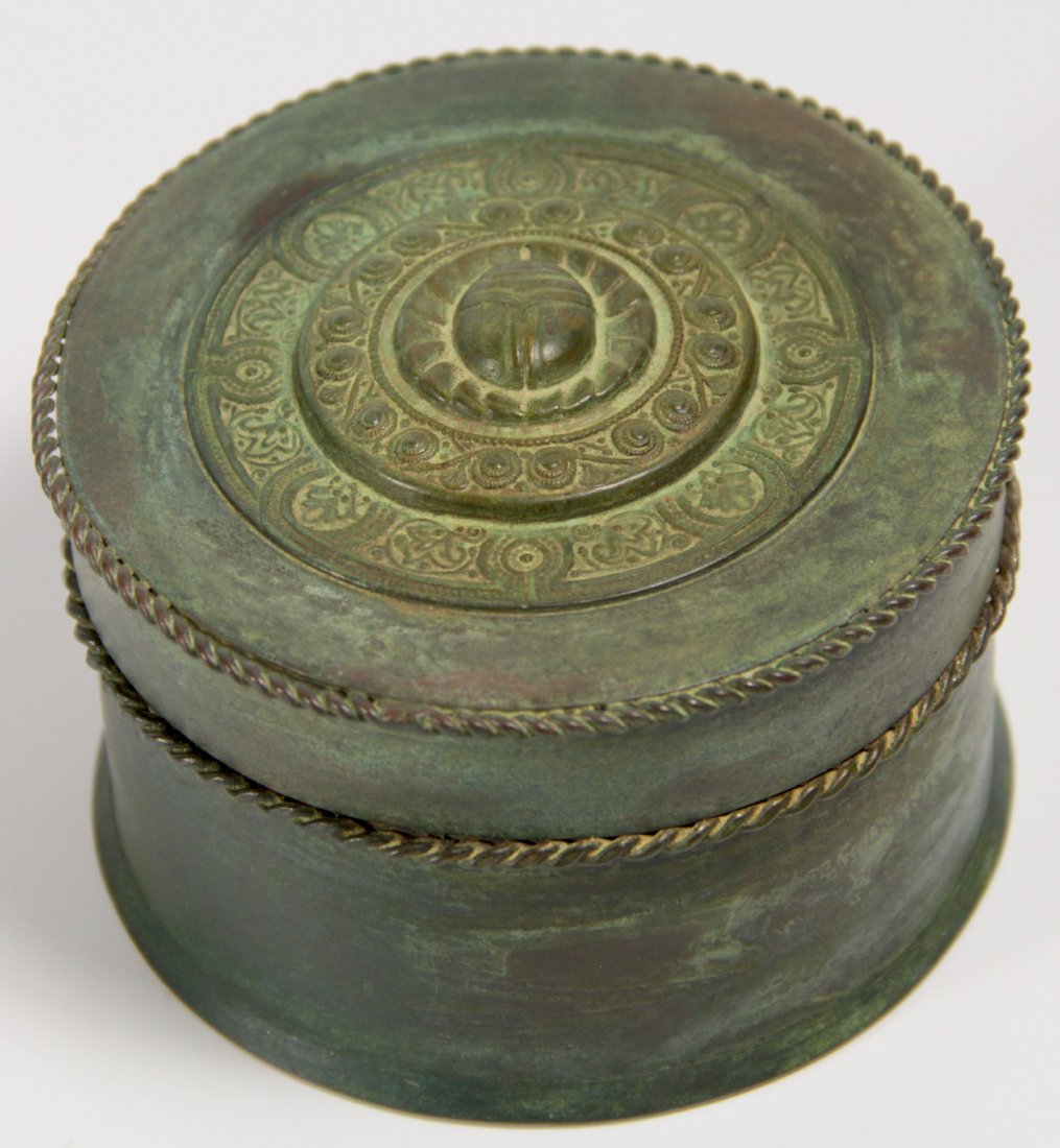Tiffany Studios Scarab Box, C. 1900: Title & Description: This patinated bronze box is perfectly cylindrical, with two braided rope designs marking the rim of the lid. On the top of the lid is a series of concentric circles, each rising 