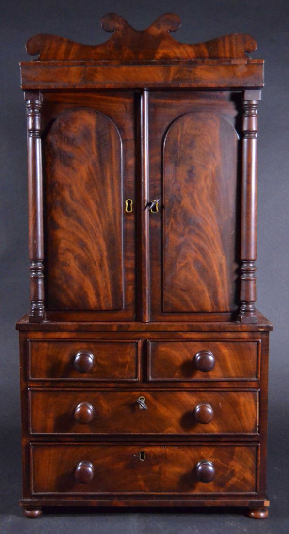 Fine Miniature Linen Press, c. 1830: Description: Constructed of Mahogany solids & oak secondary wood. Has classical turned columns, turned pulls, bun feet & carved crest, door panels are arched, raised & applied select grain mahogany. I