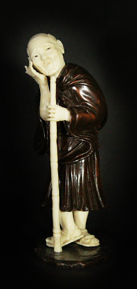Figurine, Man With Hand to Face & Staff, 19thC: Description: A Chinese carved ivory and wood figure of a man holding a staff in his left hand , while the other is rested on his cheek. Wearing traditional robes and sandals on his feet. Material: Ivo