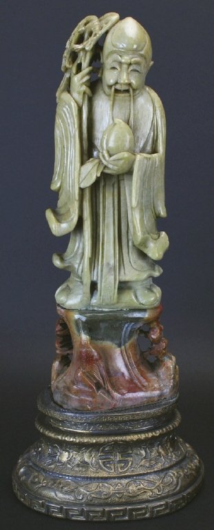 Chinese God of Longevity Shou Lao, Soapstone: Description: Carved out of green soapstone, the Chinese God of Longevity Shou Lao holding a peach, with soapstone stand and then attached on a metal stand with Chinese letters and flowers. History: Sh