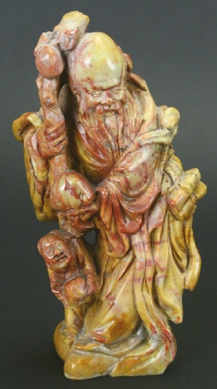 Chinese Soapstone Carving, God of Longevity: Description: A Chinese carving of the God of Longevity, Shou Lao. He is standing with a peach and staff in hand. A smaller man beneath the peach, with a peach in hand. Fine detail on a caramel rust co