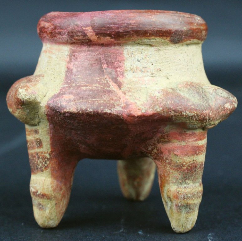 Pre-Columbian, Mayan Poison Pot, Terracotta: This pot is beige and red on three narrow legs. It has few adorning features, the most striking being the striping on the legs and the bulge of the lip.