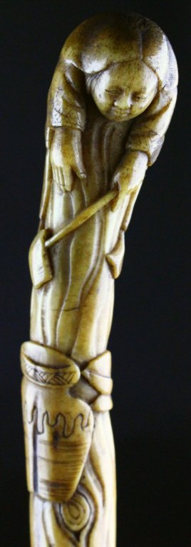 Cane, Japanese, Mahogany, 19th C.: This cane or walking stick has a head depicting a Japanese woman leaning over a stump with a long ladle to pull water from a pot on the ground beside the base of the stump. It is affixed to the shaft
