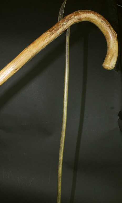 Gadget Cane, Oak, Gun Stand, C. 1900: This oaken branch wood cane or walking stick is a typical hooked cane apart from the brass bar along its length that extends outward from the shaft to become a level stand for aiming a long barreled g