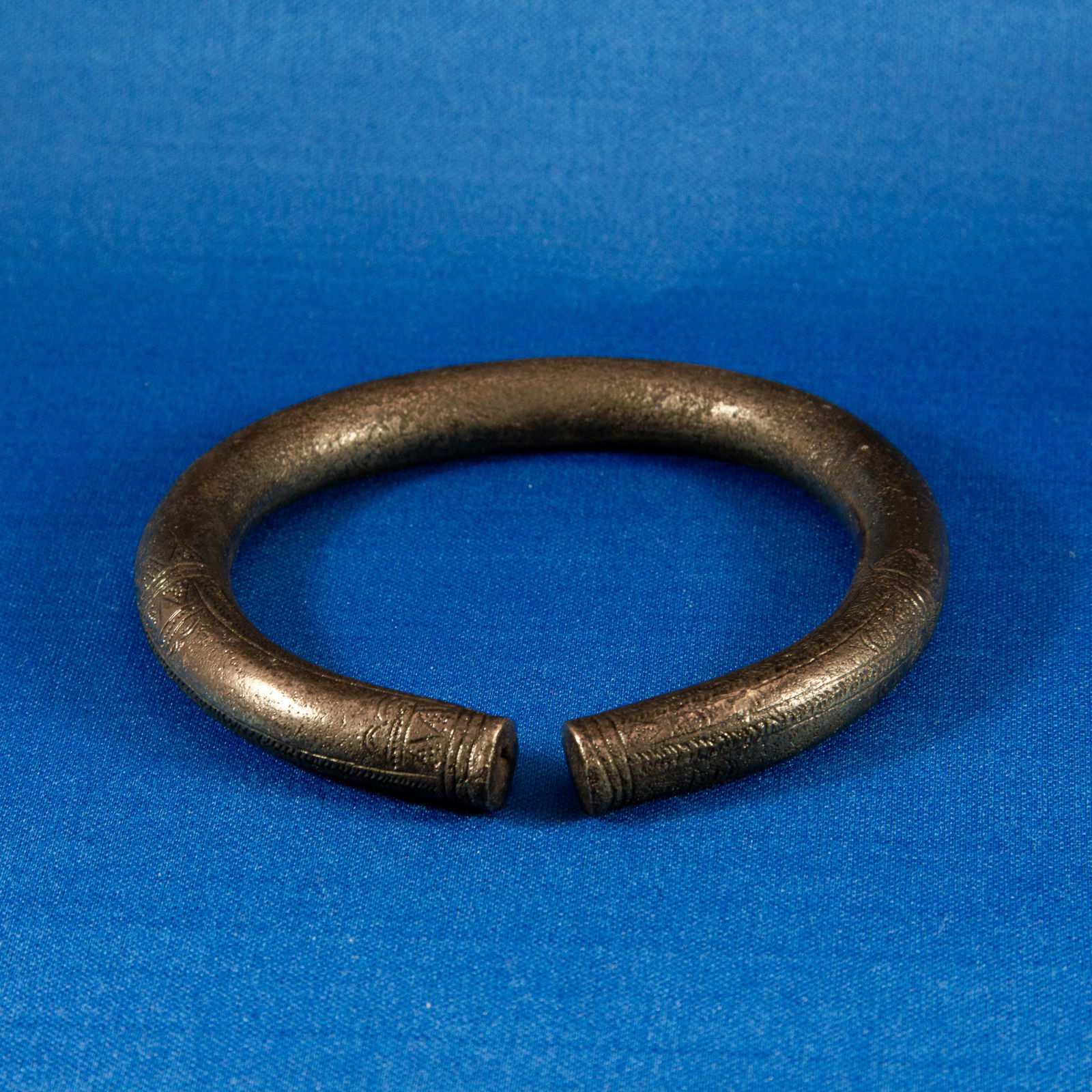 ANKLET: GEOMETRIC LURISTAN (1000-500 BC): A Luristan bronze anklet cast in a thick, heavy round-section form and shaped into a broad penannular hoop suitable for wear at the ankle rather than the wrist. The surface bears finely incised geomet