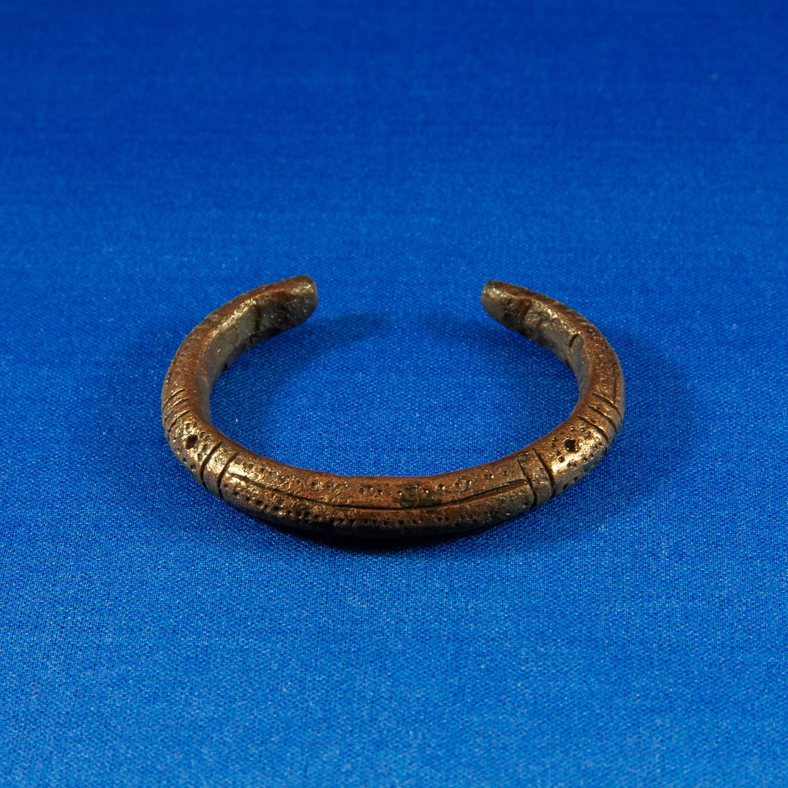 BRACELET: GEOMETRIC LURISTAN (1000-500 BC): A Luristan bronze bracelet cast in a thick, rounded profile and shaped into a compact penannular cuff. The outer surface retains its original incised linear bands and geometric designs throughout. The