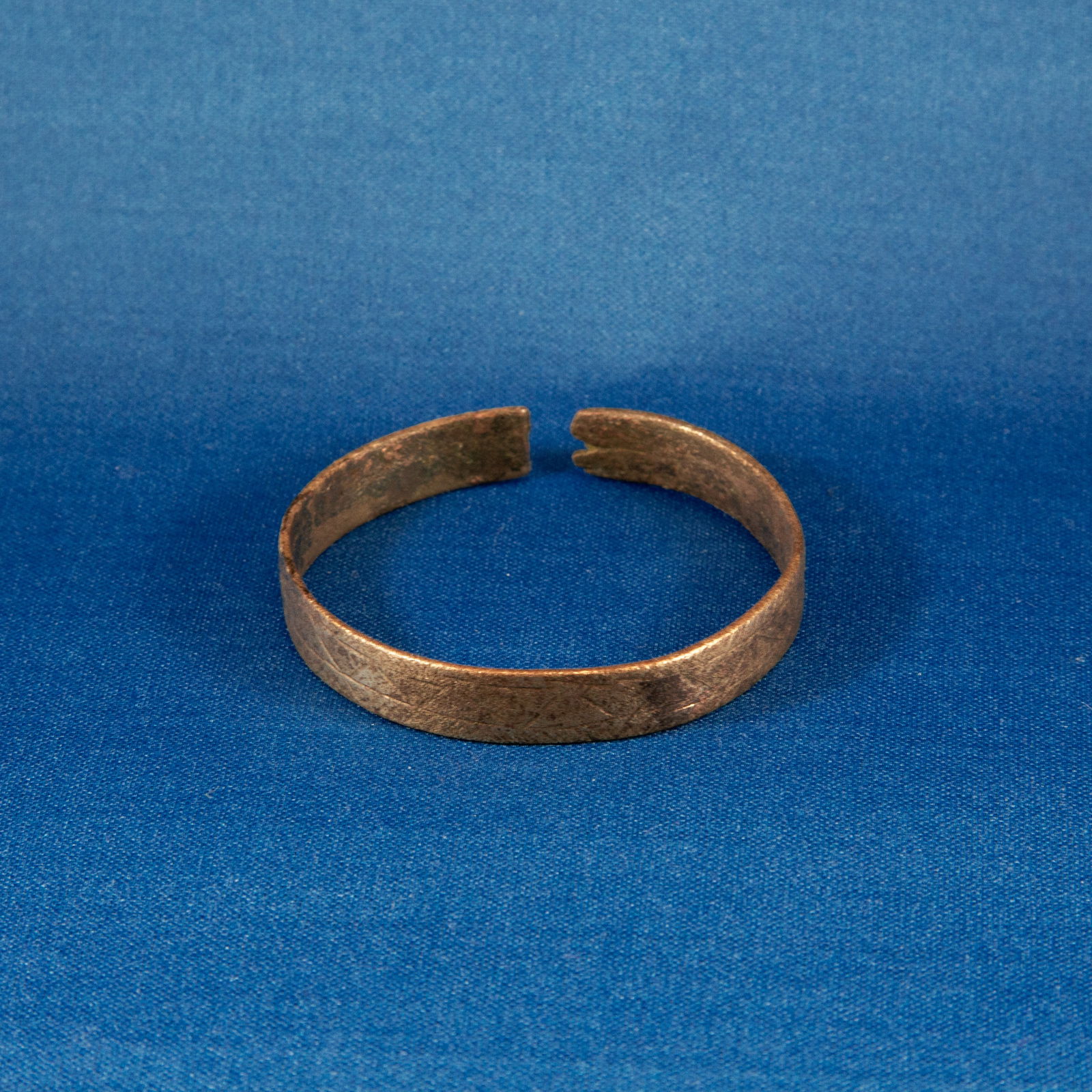 BRACELET: GEOMETRIC LURISTAN (1000-500 BC): A Luristan bronze bracelet formed from a hammered bronze strip shaped into a compact penannular cuff. The band is flat in section and decorated with a continuous incised chevron-and-triangle frieze en