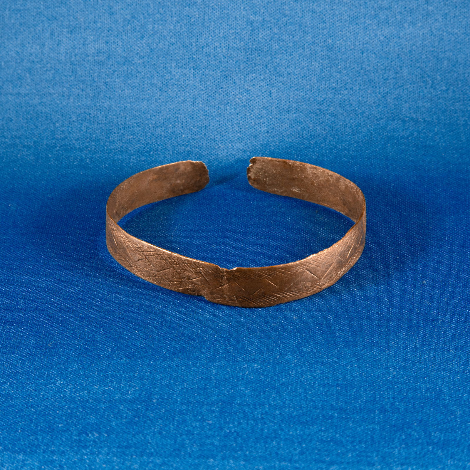 BRACELET: GEOMETRIC LURISTAN (1000-500 BC): A Luristan bronze bracelet fashioned from a hammered bronze strip formed into a penannular cuff. The band is flat in section and decorated on its exterior with a field of incised cross-hatched lines,