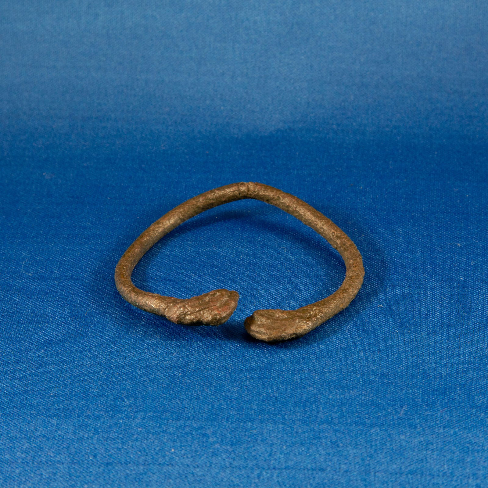BRACELET: ZOOMORPHIC BRONZE AGE (2000-300 BC): This bracelet was formed from a round-section bronze rod bent into a penannular hoop and terminating in a pair of stylized gryphon heads. The terminals, though softened by age and heavy patination, st