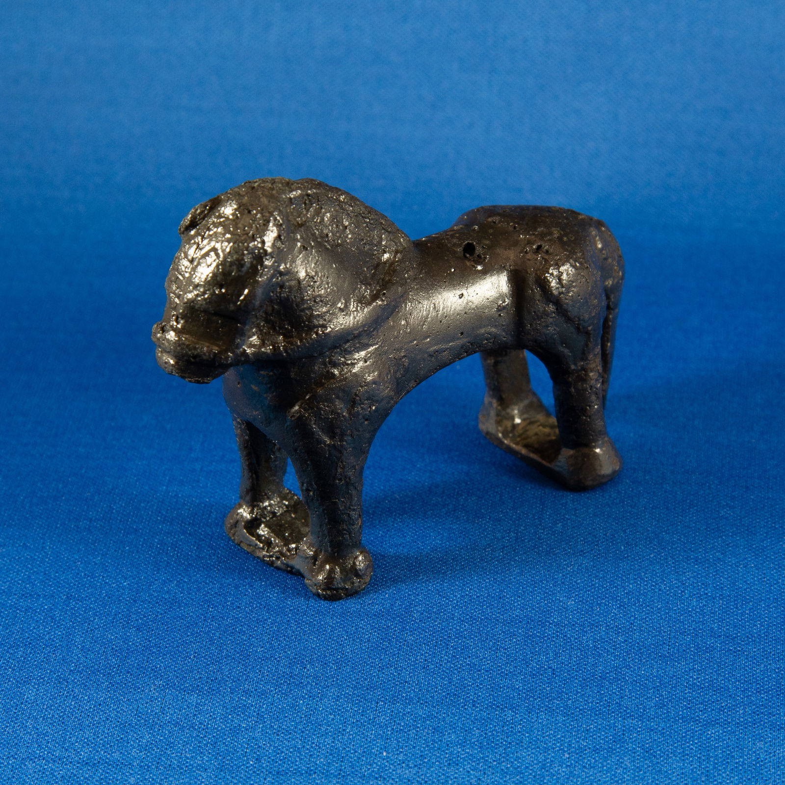 FITTING: HORSE LURISTAN (1000-500 BC): A cast leaded bronze horse figurine rendered in a compact, geometric form, standing with all four legs planted on rectangular panels that provide stability and balance. The prominent bridle and reins