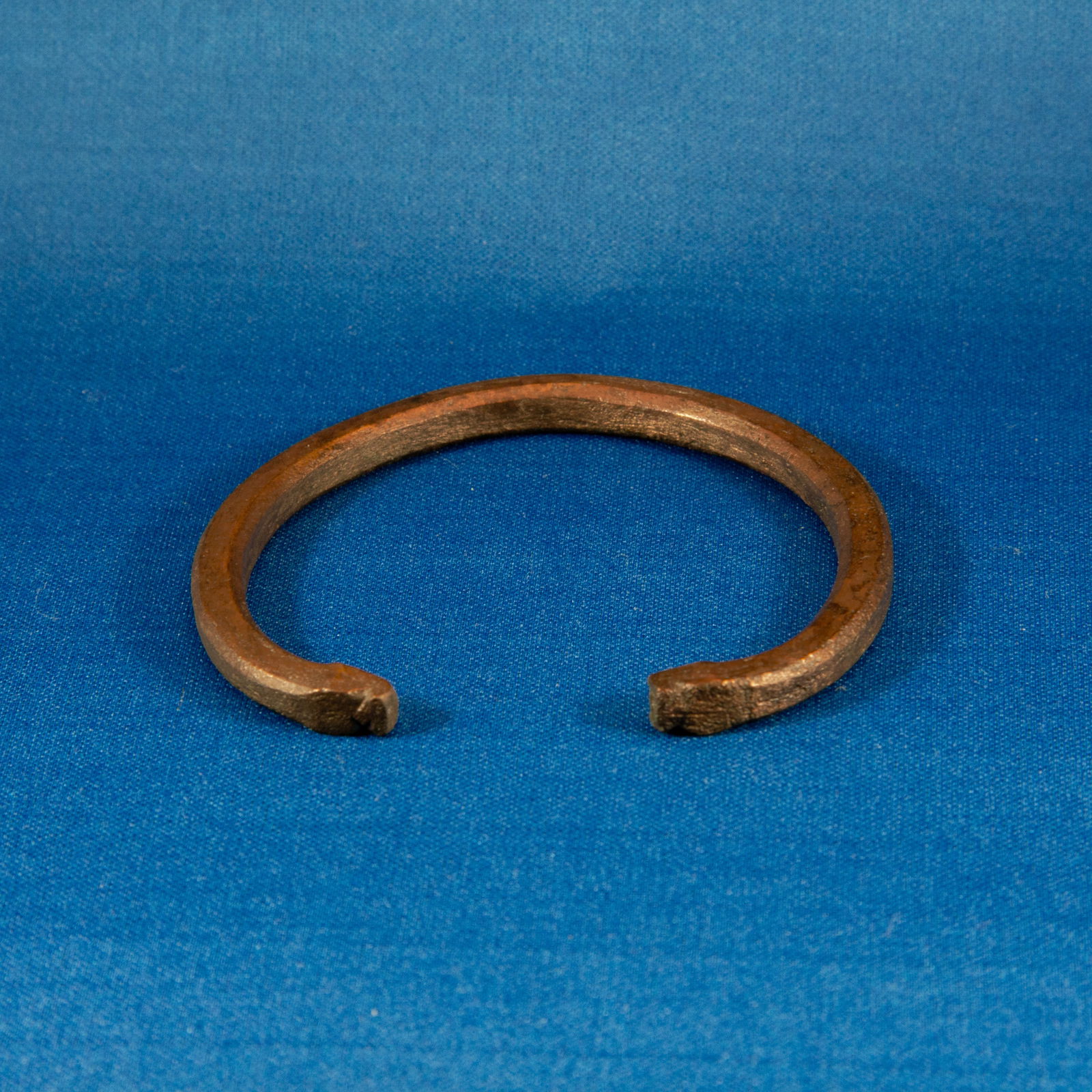 BRACELET: PENANNULAR ACHAEMENID (553-330 BC): A solid bronze penannular bracelet dating to the Achaemenid period, cast from a thick round-section bronze rod and formed into an open hoop with squared, slightly flattened terminals. The surface show
