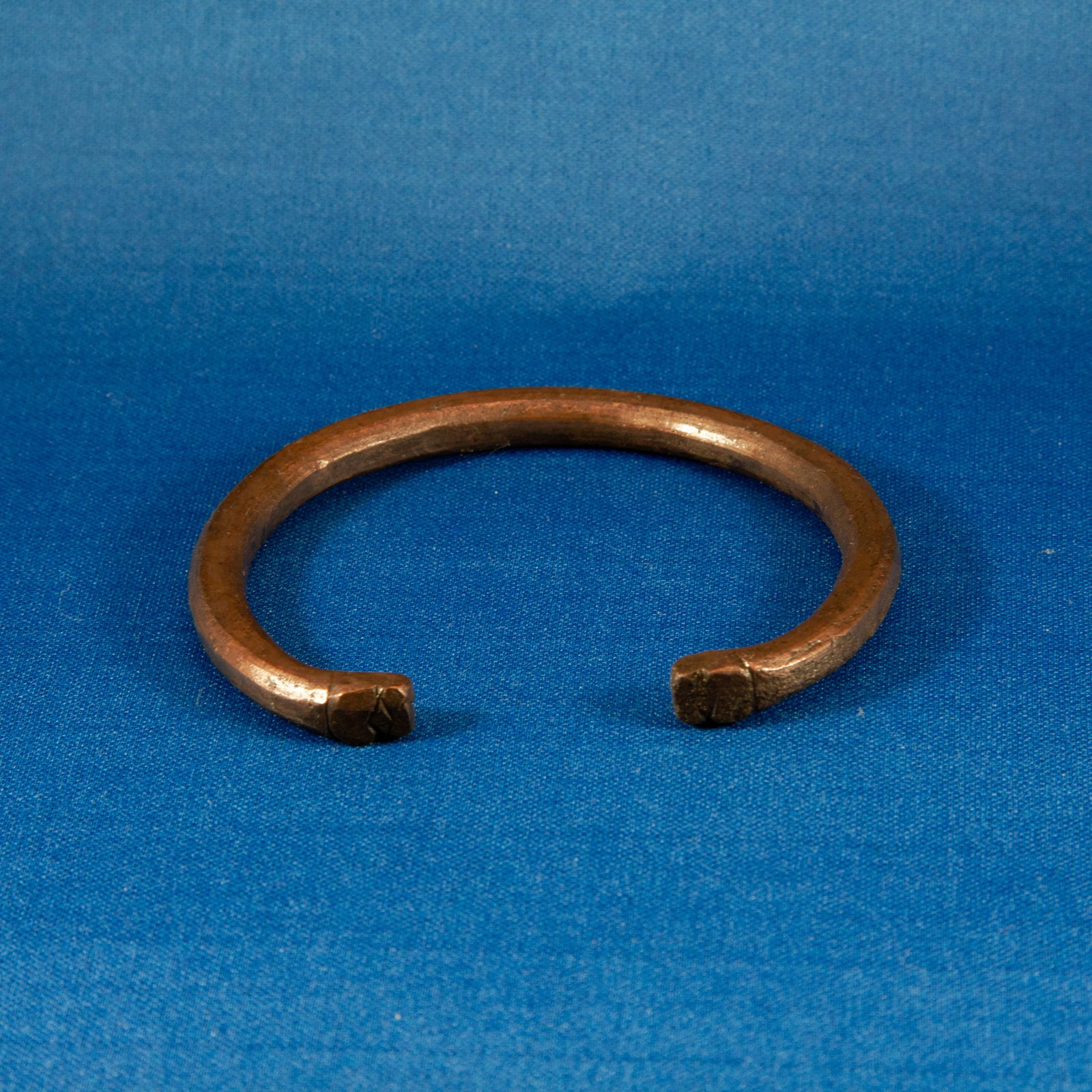 BRACELET: PENANNULAR ACHAEMENID (553-330 BC): A solid bronze penannular bracelet dating to the Achaemenid period, cast from a thick round-section bronze rod and formed into an open hoop with squared, slightly flattened terminals that bear simple