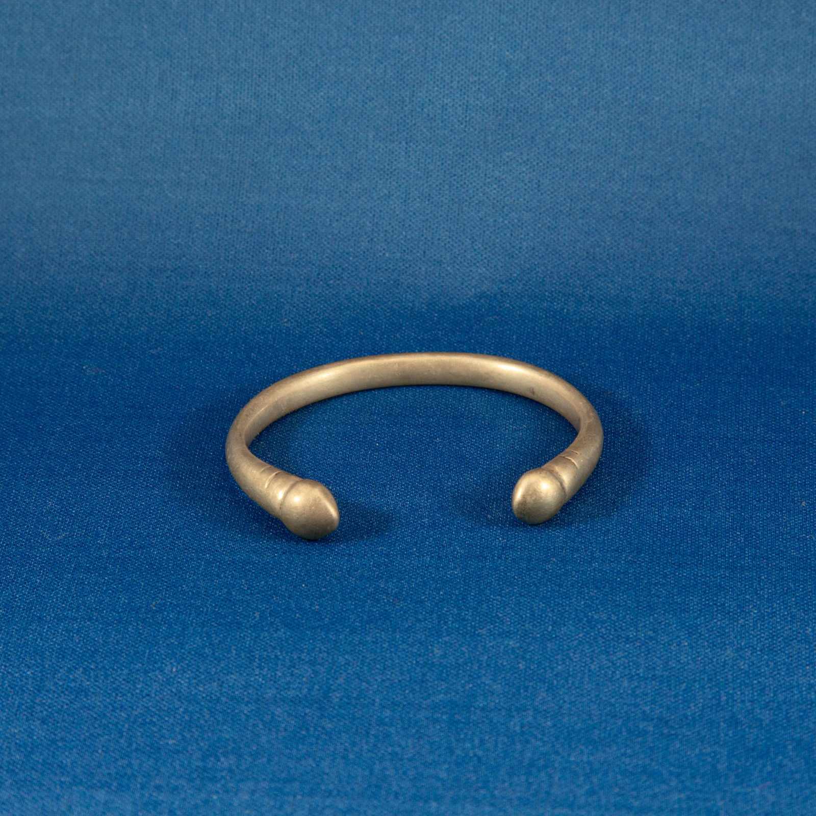 BRACELET: SILVER SASANIAN (224-651 CE): A solid silver Sasanian penannular bracelet dating to the 2nd–7th century AD, formed from a round-section silver rod bent into an open-ended hoop with smoothly rounded, globular terminals. The surfa