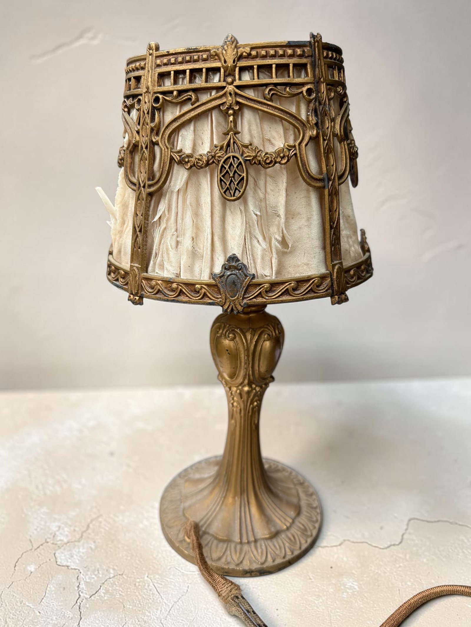 Small Ornate Metal(bronze?) Lamp and Fabric-lined Shade: Small Ornate Metal(bronze?) Lamp and Fabric-lined Shade. Fabric is worn and dusty. Wiring looks unsafe. That being said, this is a beautiful example of the Art Deco period. 12”tall. .>>>>>>>>>>>