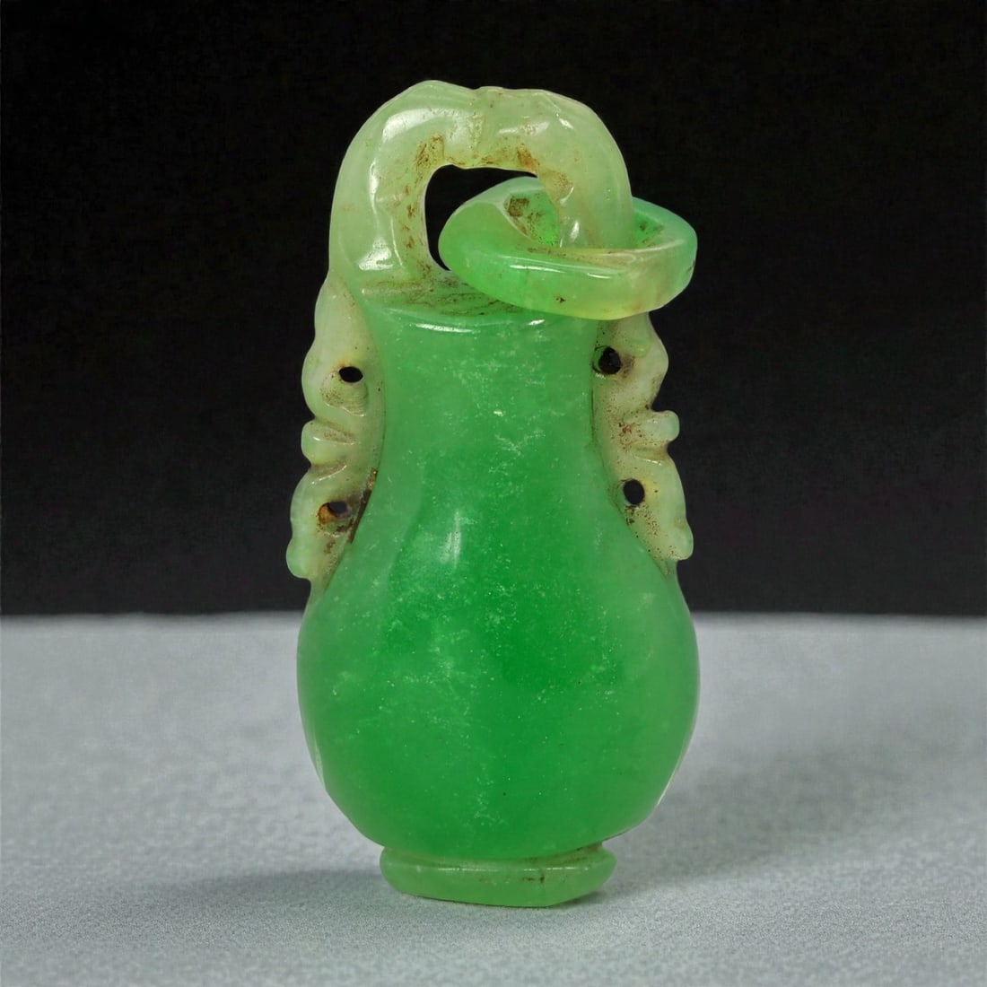 A Chinese Jadeite Jade Miniature Vessel, 20th Century, 4FD: Carved from translucent green jadeite with areas of lighter mottling and scattered brown surface inclusions, the miniature vessel is worked in the round with a softly rounded body tapering to a short
