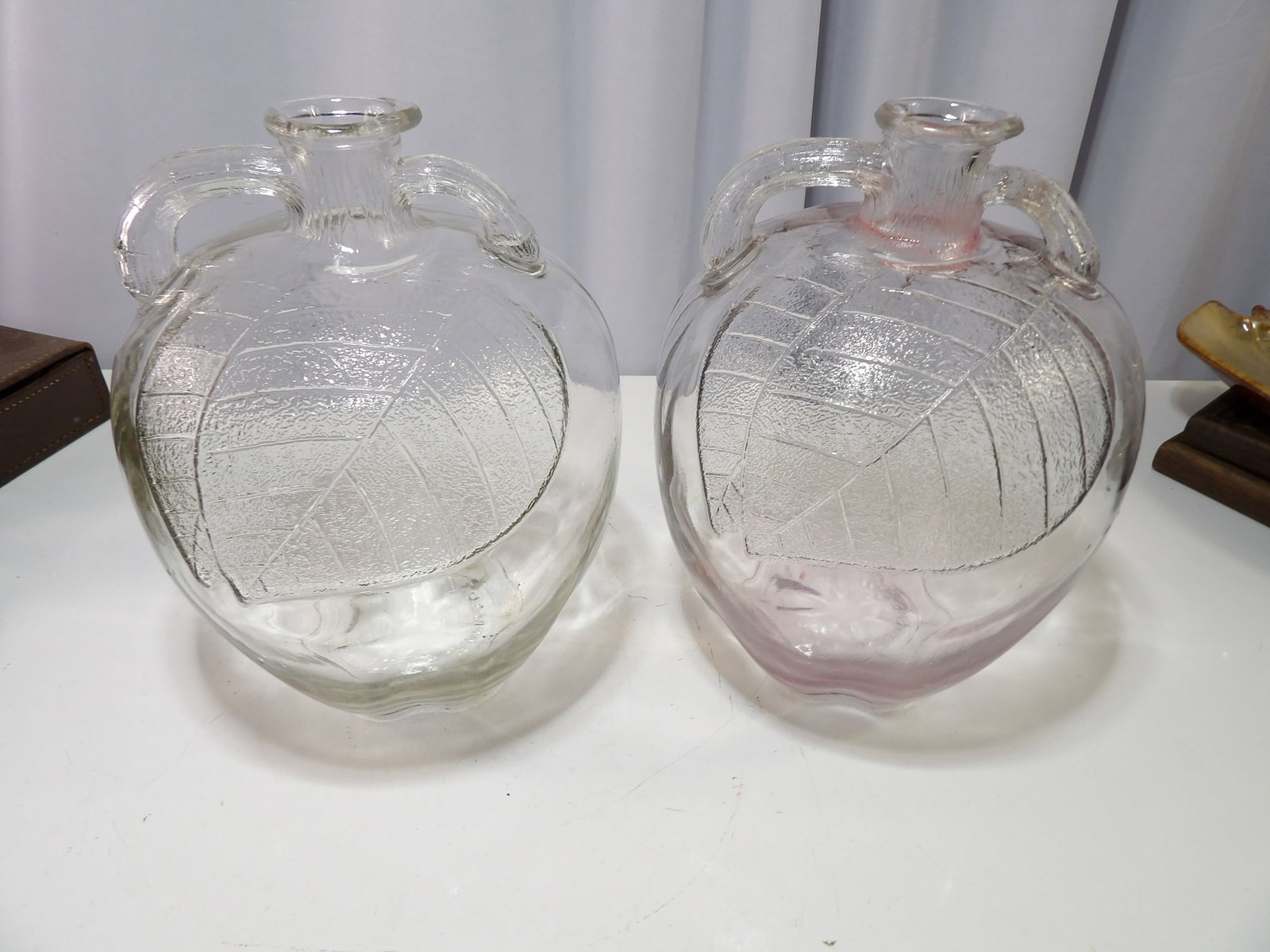 Pair of Clear Glass Apple Shaped Jugs: Pair of Vintage Clear Glass Apple Shaped Jugs with Embossed Leaf Design. All measurements approximate. Please see photos for condition and details. Selling as is from 04281.