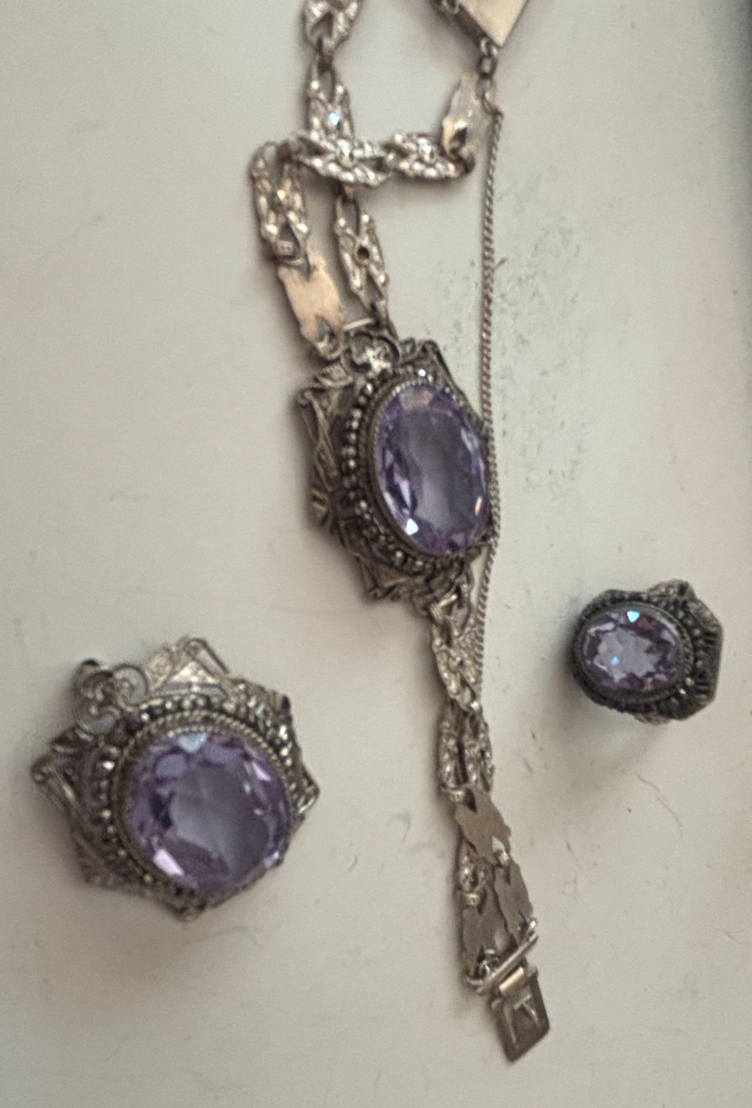 Art Deco Amethyst and Sterling Silver Jewelry Set: This jewelry set includes a bracelet and a ring, both featuring oval-cut amethyst gemstones set in sterling silver. The metalwork exhibits intricate filigree and geometric patterns characteristic of