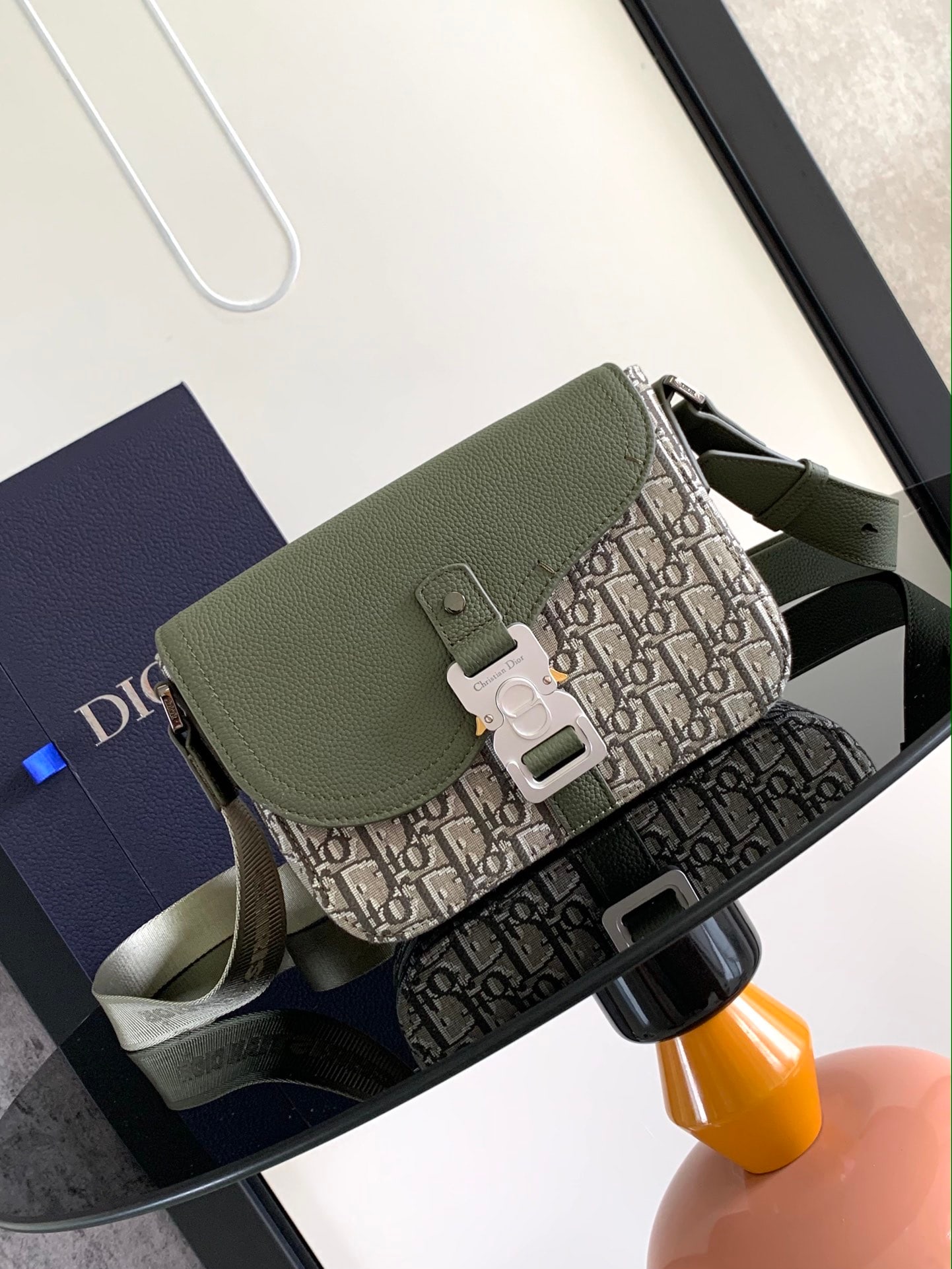Christian Dior Oblique: The small saddle messenger bag features a sleek and stylish flap design. Crafted from khaki Oblique printed fabric, it boasts a tonal grained calfskin saddle flap and is accented with aluminum hardwar