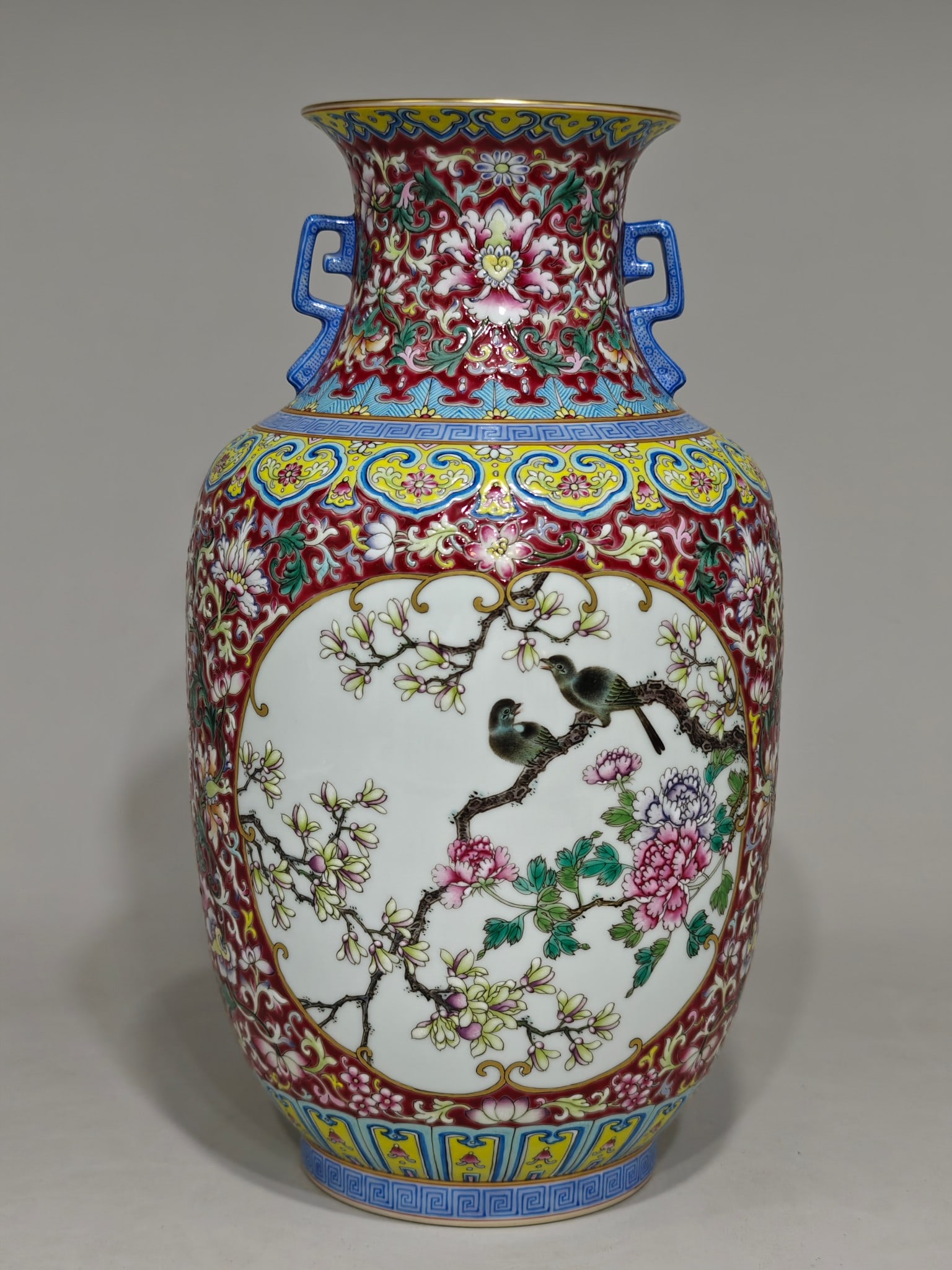 A famille rose vase with a rouge-red design featuring openwork floral and bird patterns, bearing the: two-eared vase with a famille rose enamel design in rouge red, featuring a floral and bird motif with a window pattern, and bearing the mark of the Qianlong period of the Qing Dynasty. The vase measur