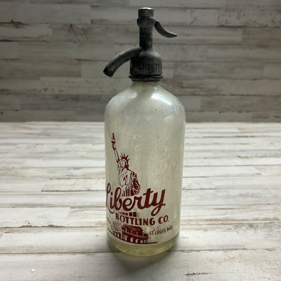Antique Liberty Bottling Co. Seltzer Bottle St. Louis MO Glass Soda Syphon: This vintage seltzer bottle features the iconic Liberty Bottling Company branding from St. Louis, Missouri. The clear glass bottle is adorned with a red graphic of the Statue of Liberty and the compan