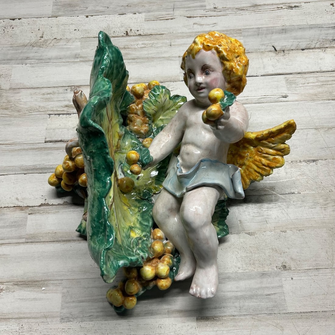 Capodimonte Angel Cherub Figurine w/ Grapes & Leaves Ceramic - Made in Italy: An exquisite ceramic figurine depicting a cherubic angel or putto nestled amongst lush grapes and detailed leaves. The angel has bright yellow hair, rosy cheeks, and is holding a cluster of small yell