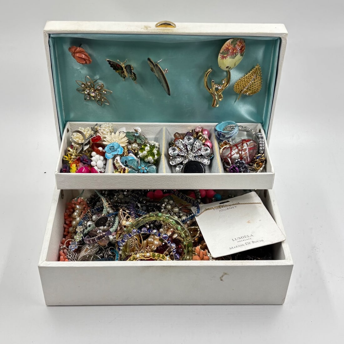 Costume Jewelry Collection w/ Trifari Brooch, Rhinestone Pieces, & Lumiela Necklace: A curated collection of costume jewelry housed within a white textured jewelry box featuring two tiers. The top lid showcases decorative pins including a Trifari butterfly brooch, a floral pin with rh