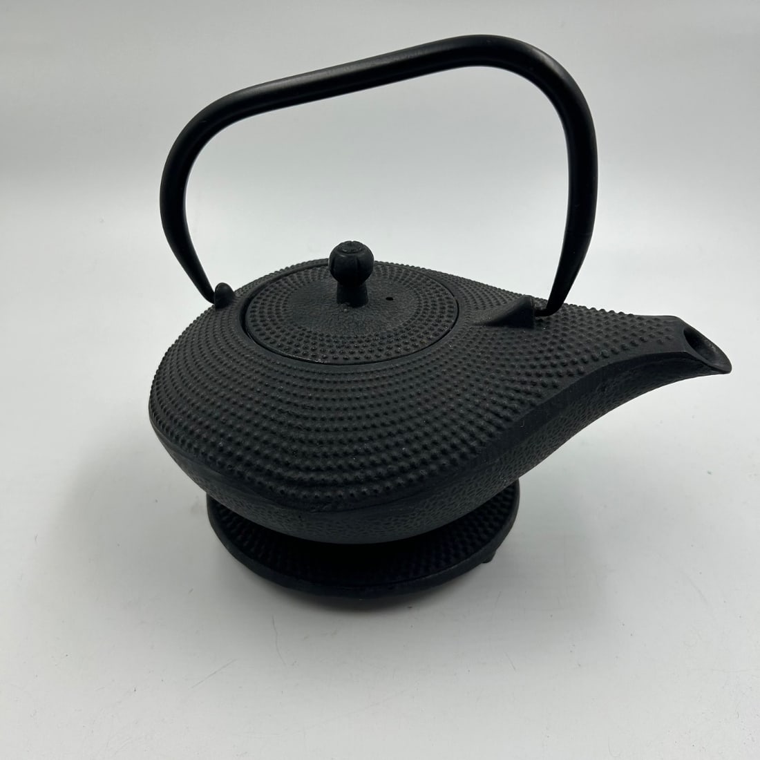 Cast Iron Tetsubin Teapot & Trivet Set - Asian Style "Hobnail" Pattern: This cast iron tetsubin teapot and trivet set features a classic Asian-inspired design with a distinctive "hobnail" texture across its surface. The teapot has a graceful pouring spout, a sturdy arched