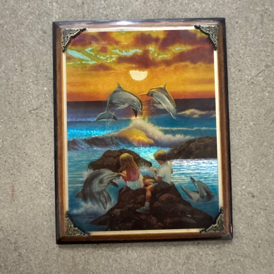 Vintage "Dolphins at Sunset" Mirrored Art Glass Plaque with Children: This charming vintage art plaque features a vibrant scene of dolphins leaping in the ocean at sunset, with two children sitting on rocks. The artwork is printed on mirrored glass, creating a unique de