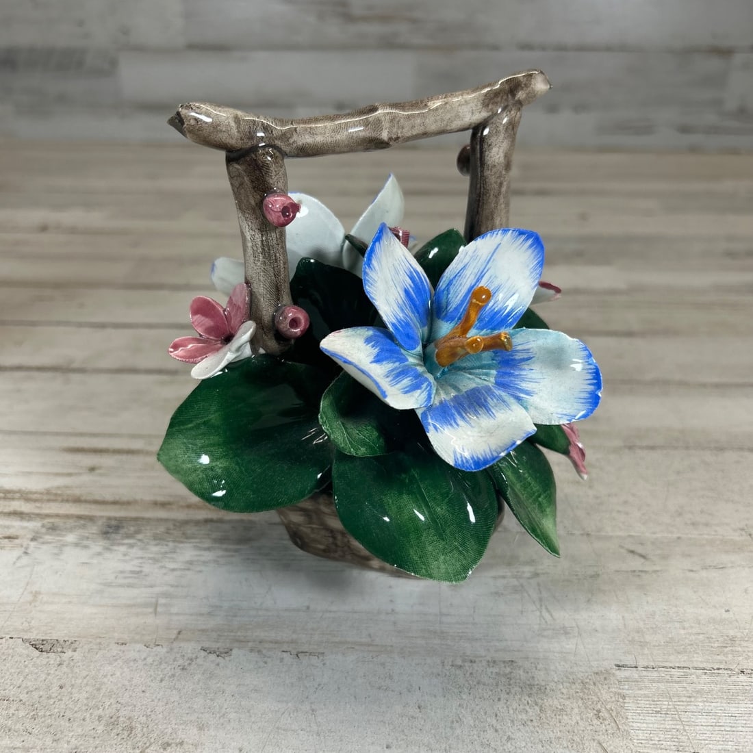 Capodimonte Italy Ceramic Flower Basket Figurine Blue White Flowers: Exquisite vintage Capodimonte ceramic figurine depicting a charming flower basket overflowing with vibrant blue, white, and pink blossoms. The basket features a rustic branch-like handle and is adorne