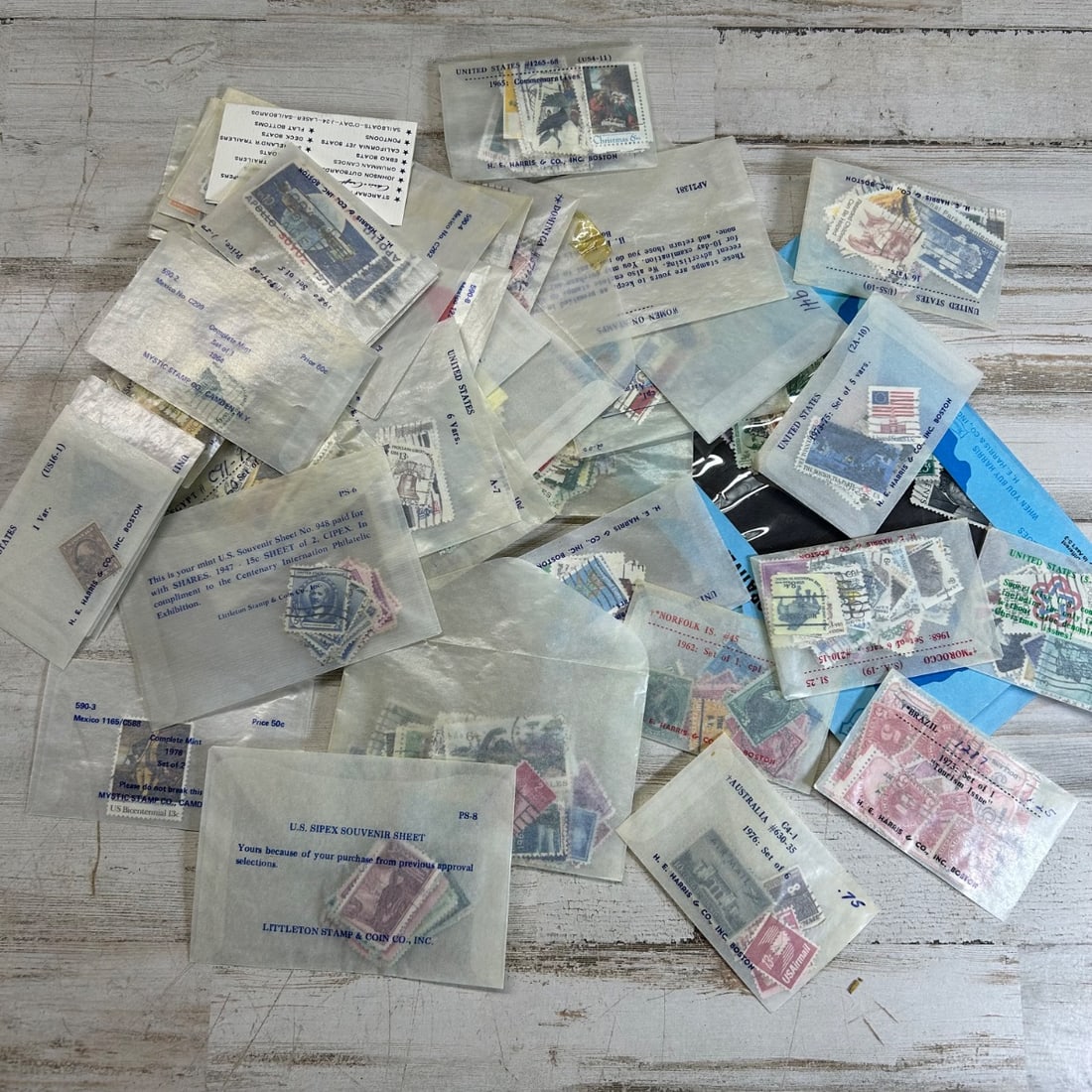 Assorted US & International Postage Stamps Collection - H.E. Harris, Littleton, Mystic: This collection features a diverse array of United States and international postage stamps, primarily housed in cellophane envelopes from reputable dealers such as H.E. Harris & Co., Littleton Stamp &