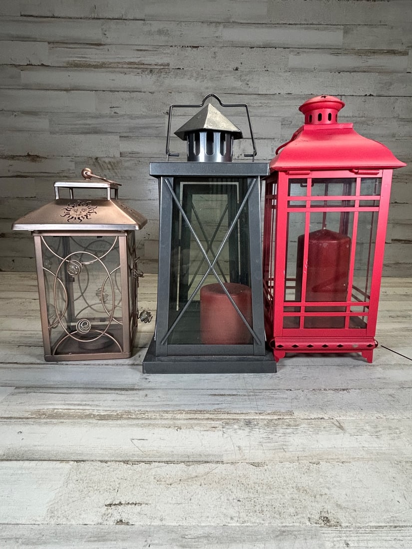 Lot of 3 Decorative Metal Lanterns with Candles - Vintage Farmhouse Style: This lot features three decorative metal lanterns, perfect for adding vintage farmhouse charm to any indoor or outdoor space. The collection includes a copper-toned lantern with intricate scrollwork a