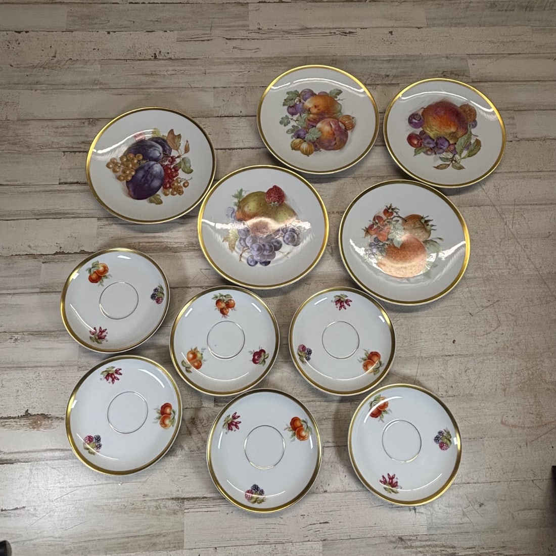 Porcelain Fruit Plates & Saucers Set - E&R JAEGERSLO C 1950's: This collection features a set of 7 porcelain plates, each adorned with vibrant fruit motifs, and 4 matching saucers. The pieces are decorated with detailed renderings of plums, pears, apples, peaches