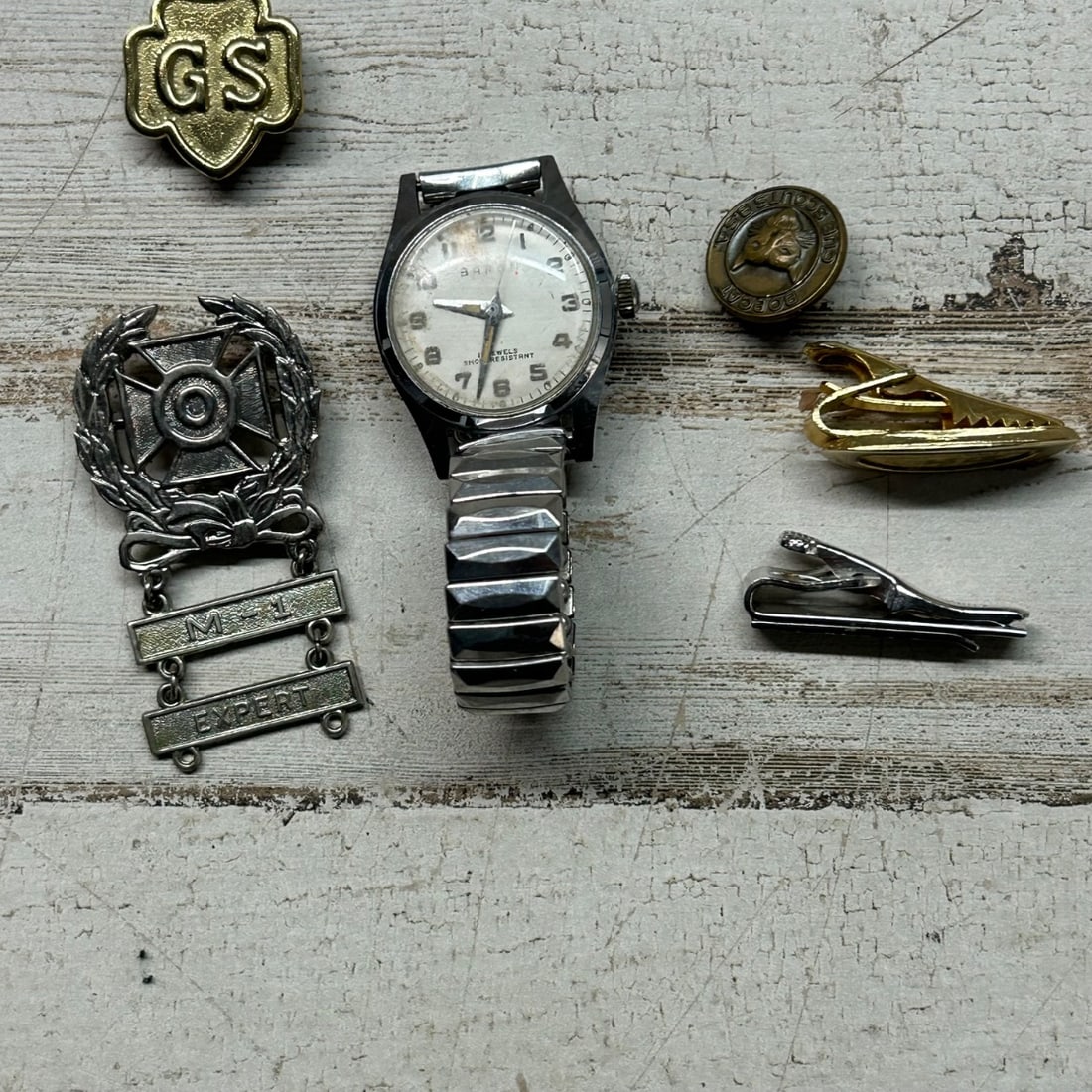 Vintage Watch, BSA Merit Badge, GS Pin, Tie Clip Assortment: This collection features a vintage Baron watch with a white dial and expandable metal band. Accompanying the watch are several collectible pins and accessories, including a gold-tone Girl Scout (GS) p