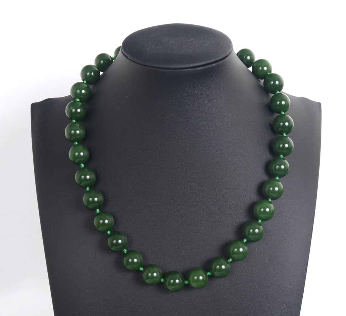 Chinese Dark Green Jade Style Necklace: Gorgeous Chinese dark green jade style beaded necklace comprised of thirty perfectly polished spherical beads throughout. Strung together with a bright green silk style thread with a silvered clasp.