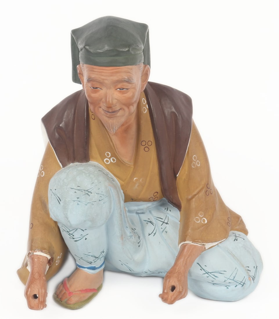Japanese Ceramic Figure, Musician, ex-Andrew Jones: Japanese ceramic painted figure of a man depicted kneeling with hands gripped, he would have been holding drumsticks. He is wearing mustard yellow top with light blue pants and a grey hat, smiling