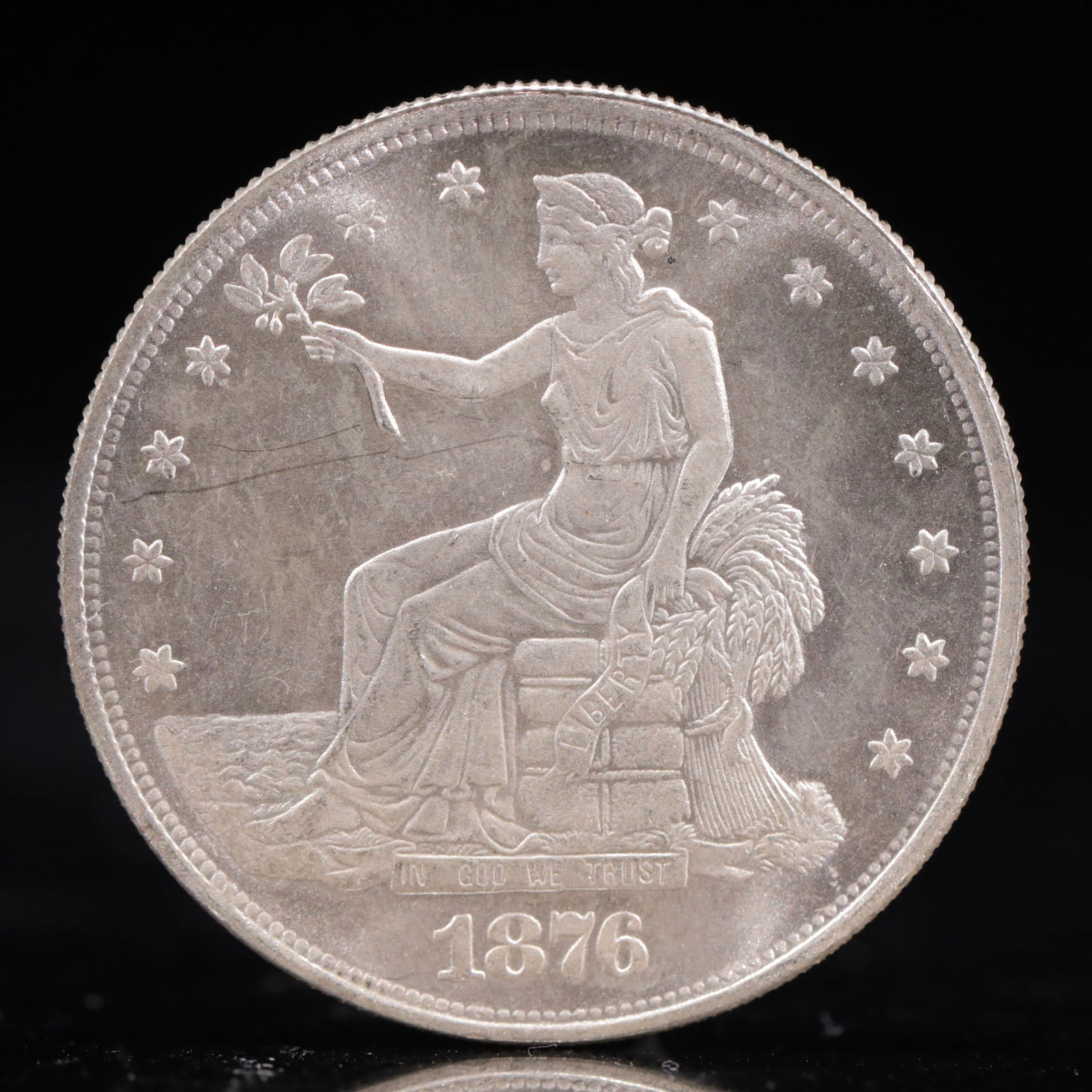 USA Trade Dollar 1876 Coin: American coin. Obverse: Liberty seated on a pedestal facing the sea to the left holding olive branches surrounded by 13 stars. IN GOD WE TRUST / LIBERTY / 1876. Reverse: An eagle holding branches