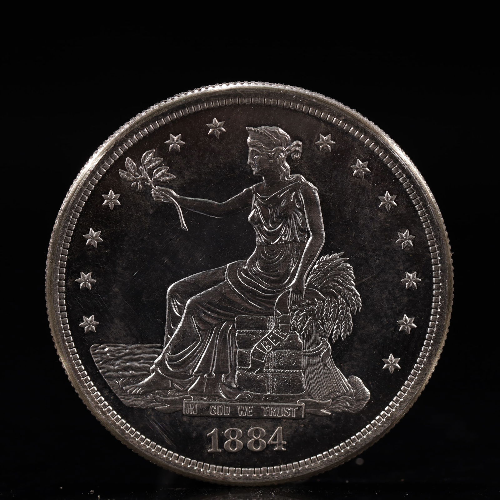 USA Trade Dollar 1884 Coin: American coin. Obverse: Liberty seated on a pedestal facing the sea to the left holding olive branches surrounded by 13 stars. IN GOD WE TRUST / LIBERTY / 1884. Reverse: An eagle holding branches with