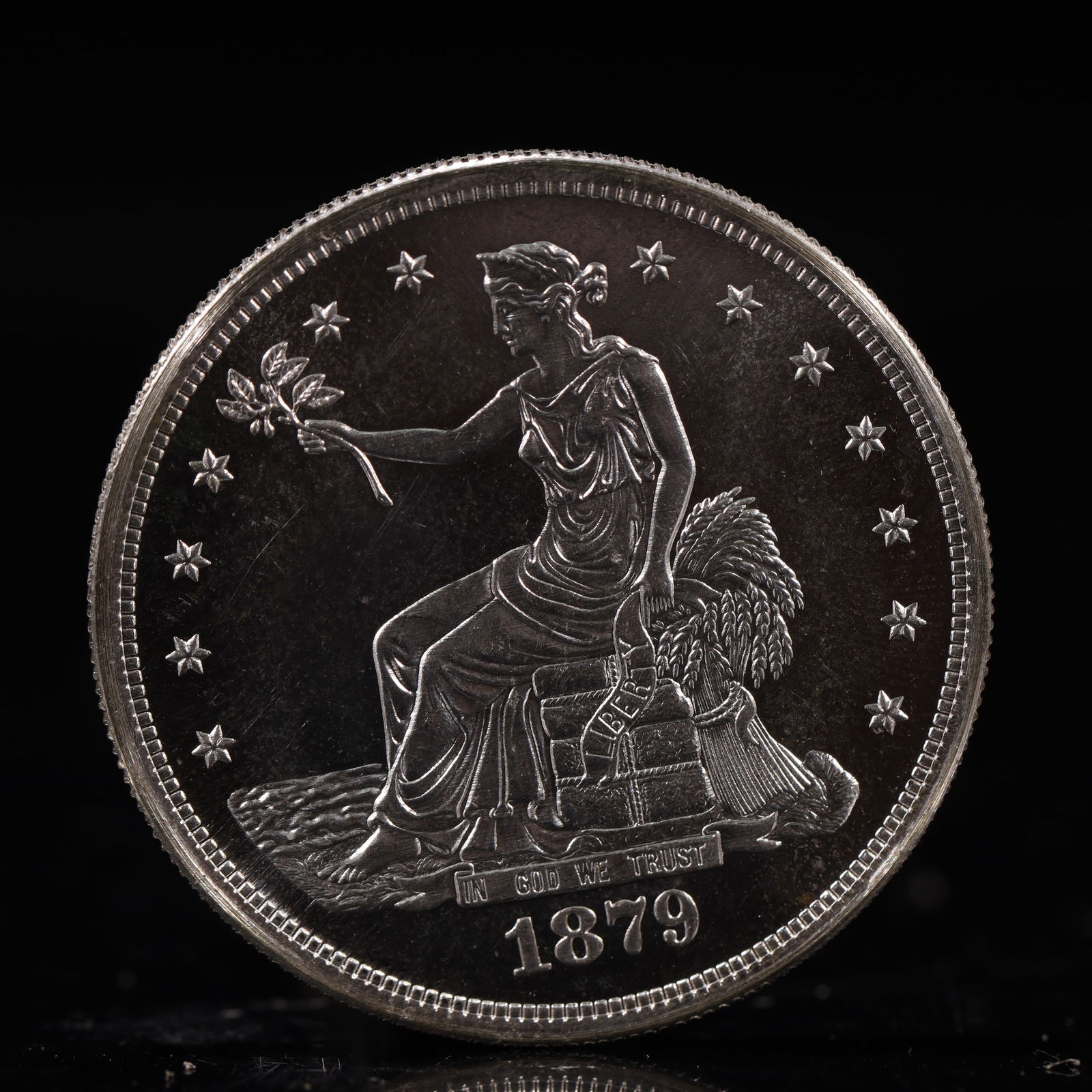 USA Trade Dollar 1879 Coin: American coin. Obverse: Liberty seated on a pedestal facing the sea to the left holding olive branches surrounded by 13 stars. IN GOD WE TRUST / LIBERTY / 1879. Reverse: An eagle holding branches with
