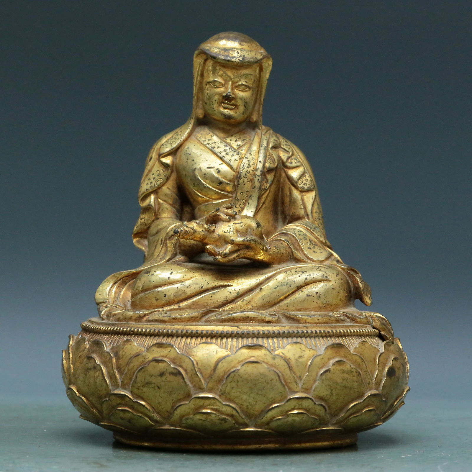 An Archaic Gilt-Bronze Figure Of Kubera: An Archaic Gilt-Bronze Figure Of Kubera. The figure is seated, body rendered clad in long, flowing robes, the voluminous drapery elegantly cascading in folds, holding a miniature mythical beast. 18th