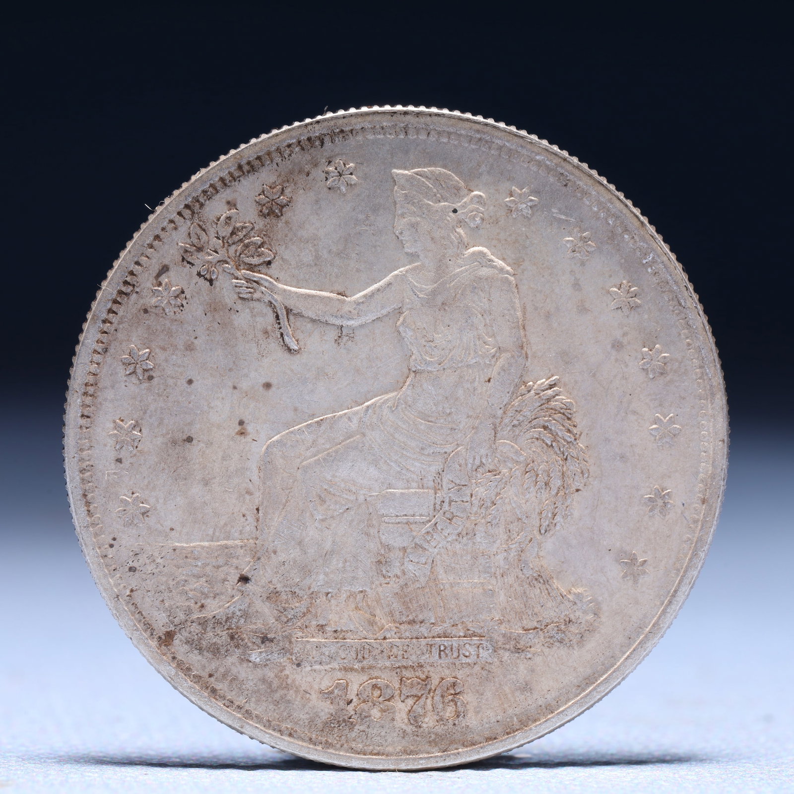 USA Trade Dollar 1876 Coin: American coin. Obverse: Liberty seated on a pedestal facing the sea to the left holding olive branches surrounded by 13 stars. IN GOD WE TRUST / LIBERTY / 1876. Reverse: An eagle holding branches with