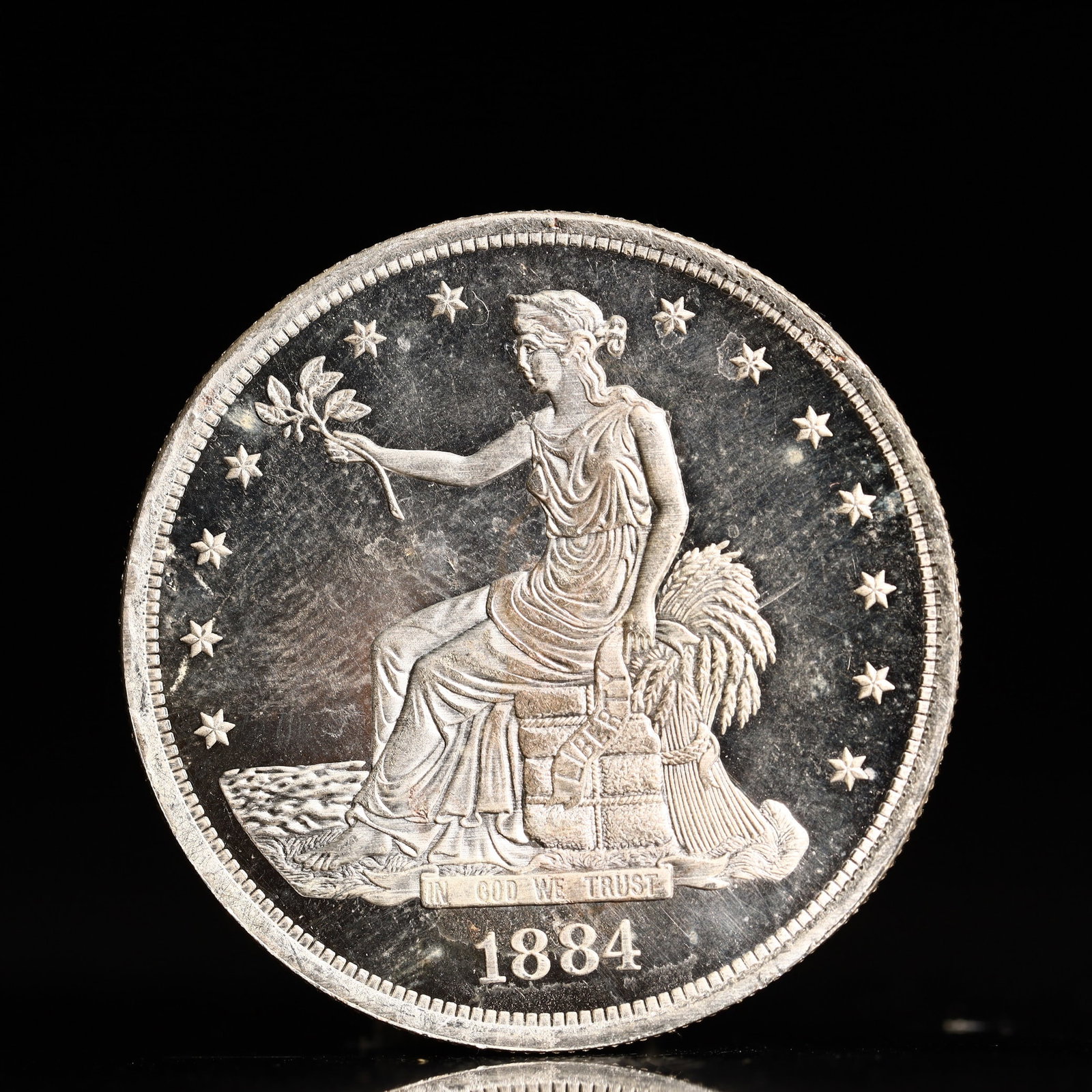 USA Trade Dollar 1884 Coin: American coin. Obverse: Liberty seated on a pedestal facing the sea to the left holding olive branches surrounded by 13 stars. IN GOD WE TRUST / LIBERTY / 1884. Reverse: An eagle holding branches with